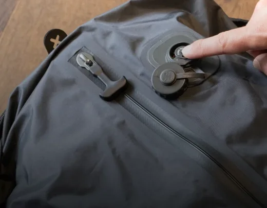 Finger pressing the built-in vacuum pump button on the Voyge backpack compression bag